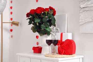 Şenlik odasında gül buketi, şarap kadehleri ve hediye kutularıyla dolu beyaz bir masa. Sevgililer Günü kutlamaları