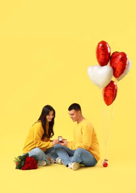 Alyansı ve sarı arka planda gül buketi olan genç nişanlı bir çift. Sevgililer Günü kutlaması