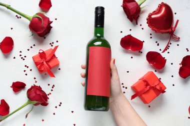 Kırmızı manikürlü kadın eli, beyaz arka planda şarap şişesi ve dekor. Sevgililer Günü kutlaması