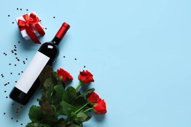 Güllü bir şişe şarap, mavi arka planda hediye ve konfeti. Sevgililer Günü kutlaması