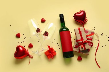 Sarı arka planda bir şişe şarap, hediyeler ve dekor. Sevgililer Günü kutlaması