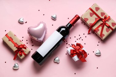 Bir şişe şarap, hediye kutuları, çikolata şekerlemeleri ve pembe arka planda kalp şeklinde balon. Sevgililer Günü kutlaması