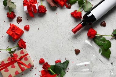 Kırmızı güllerden yapılmış çerçeve, şarap şişesi, bardak, çikolata şekeri ve beyaz arka planda hediye kutuları. Sevgililer Günü kutlaması