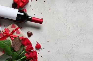 Bir şişe şarap, hediye kutuları, çikolata şekerlemeleri ve beyaz arka planda kırmızı güller. Sevgililer Günü kutlaması
