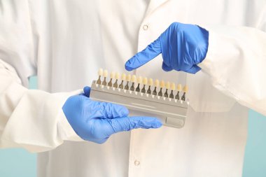 Turkuaz arka planda diş rengi örnekleri olan erkek dişçi, yakın plan.