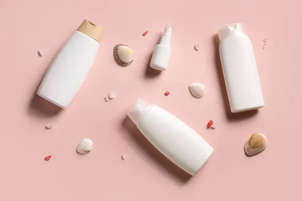Different bottles of sunscreen cream with seashells on pink background