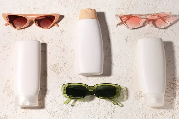 Bottles of sunscreen cream and different sunglasses on grunge white background