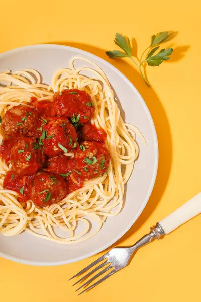 Plate of boiled pasta with tomato sauce and meat balls on yellow background