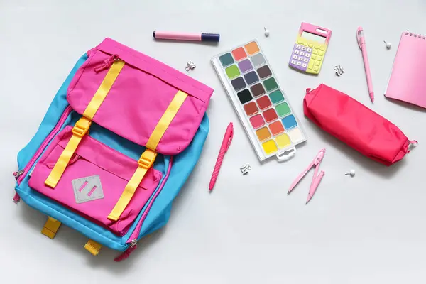 Colorful school backpack with watercolors, calculator and pencil case on white background