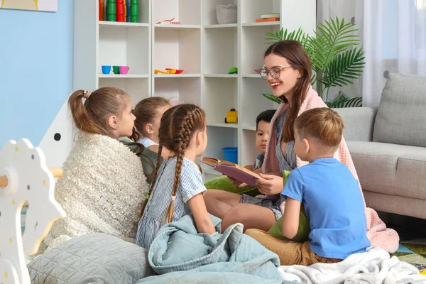 Nursery teacher reading bedtime story to little children in kindergarten