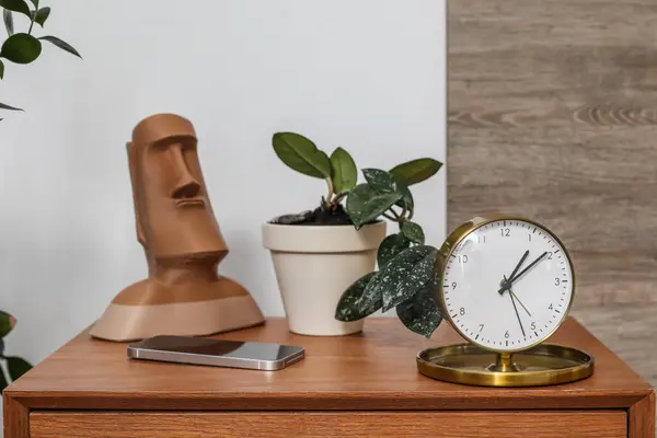Alarm clock, houseplant and mobile phone on wooden bedside table in bedroom, closeup