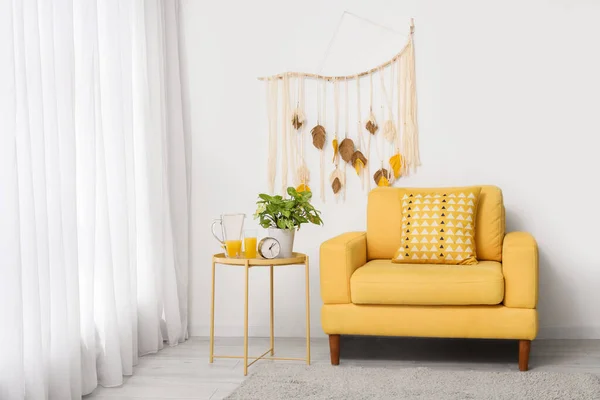 Interior of living room with yellow armchair, macrame and alarm clock on coffee table