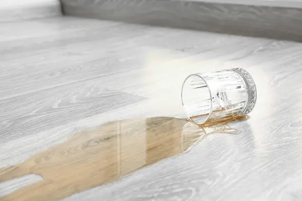 Wooden laminate floor with overturned glass of juice