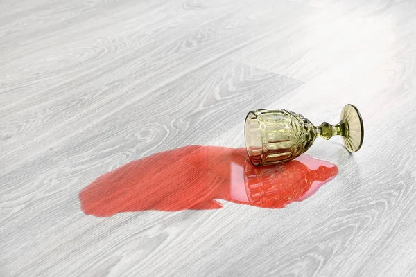 Wooden laminate floor with overturned glass of wine
