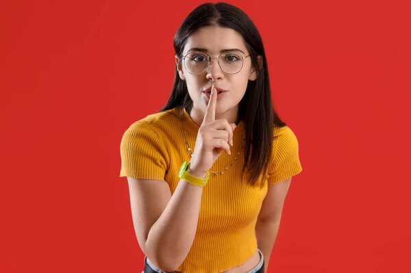 Young gossip woman showing silence gesture on red background