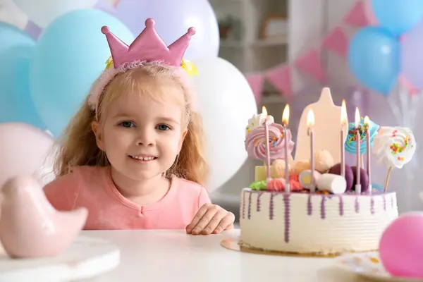 Cute little girl in crown with cake celebrating Birthday at home