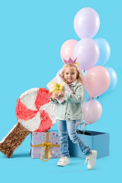 Cute little girl with Birthday gifts, candy pinata and balloons on blue background