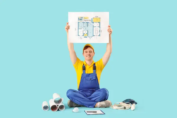 Male electrician with house plan and supplies on blue background