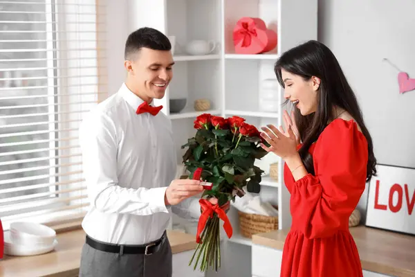 Young man with bouquet of roses proposing to his girlfriend in kitchen. Valentine\'s Day celebration