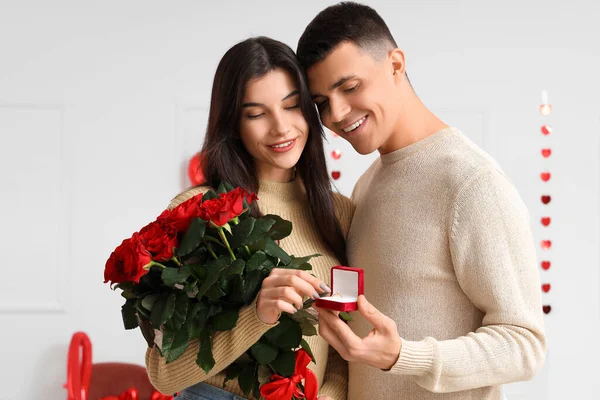 Young engaged couple with bouquet of roses in bedroom. Valentine\'s Day celebration