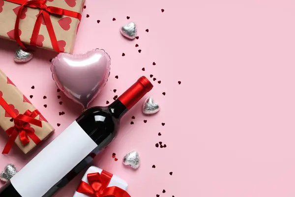 Bottle of wine with gift boxes, chocolate candies and heart shaped air balloon on pink background. Valentine\'s Day celebration