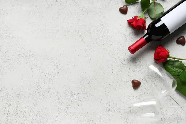 Bottle of wine with glasses, chocolate candies and red roses on white background. Valentine\'s Day celebration