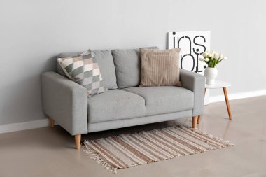 Yastıklı rahat bir kanepe ve gri duvarın yanındaki masada vazoda lale çiçekleri.