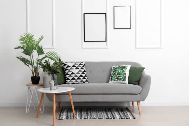 Beyaz duvarın yanındaki masalarda yastıklı ve çiçekli rahat bir kanepe.