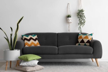 Beyaz duvarın yanında minderleri ve çiçekleri olan rahat siyah kanepe.