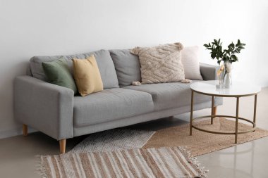 Yastıklı rahat gri kanepe ve ışık duvarının yanındaki masada vazoya ağaç dalları.