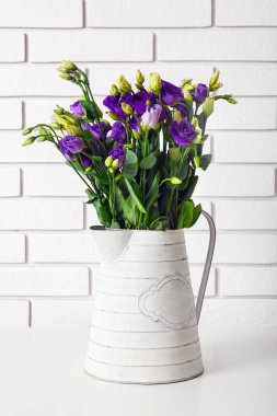 Beyaz tuğla duvarın yanındaki masada Eustoma çiçekli sürahi.