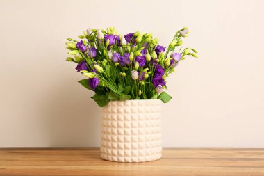 Beyaz duvarın yanındaki ahşap masada, östoma çiçekleri olan vazo.