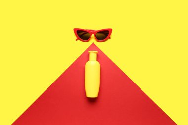 Arka planda güneş kremi şişesi olan güneş gözlüğü.