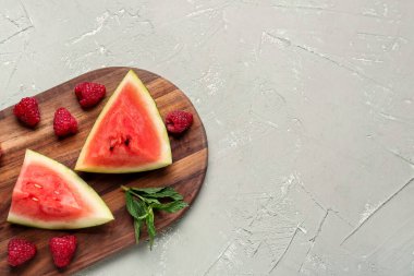 Taze karpuz parçaları ve gri arkaplanda ahududu olan tahta.
