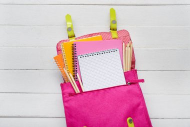 Beyaz ahşap zemin üzerinde boş defter ve kırtasiye malzemesi olan sırt çantası