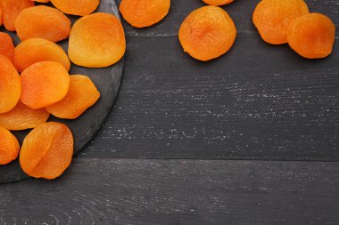 Siyah ahşap arka planda lezzetli kurutulmuş kayısıları olan tahta.