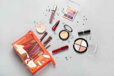 Gri arkaplanda makyaj ürünleri olan şık kırmızı kozmetik çanta