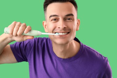 Yeşil arka planda elektrikli diş fırçası olan yakışıklı bir adam, yakın plan.
