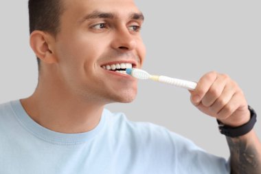 Gri arka planda diş fırçası olan yakışıklı bir genç. Diş sağlığı konsepti