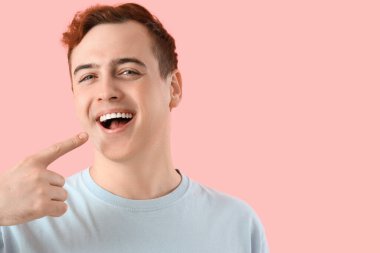 Young man pointing at his teeth on pink background, closeup