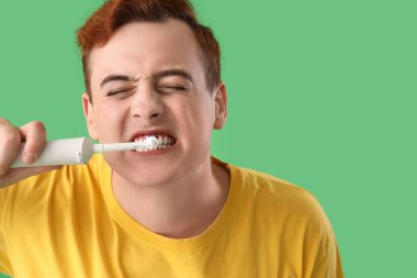 Yeşil arka planda elektrikli diş fırçası olan genç adam, yakın plan.