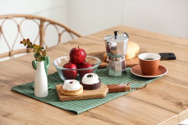 Mutfakta bir fincan kahveli ahşap masa, taze hamur işi ve elmalar, yakın plan.