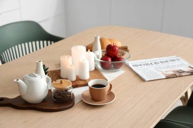 Modern mutfakta kahve, elma ve yanan mumlarla dolu ahşap masa.