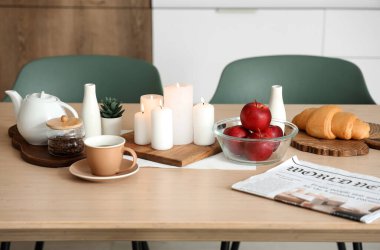Modern mutfakta kahve, elma ve yanan mumlarla dolu ahşap masa.