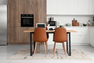 Modern mutfağın içinde dizüstü bilgisayarı, çay seti ve defter olan ahşap masa.