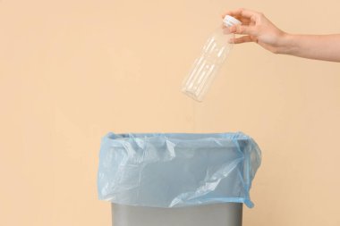Kadın eli, bej duvarın yakınındaki çöp kutusuna boş plastik şişe atıyor.