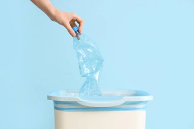 Mavi duvarın yakınındaki çöp kutusuna plastik şişe atan bir kadın.