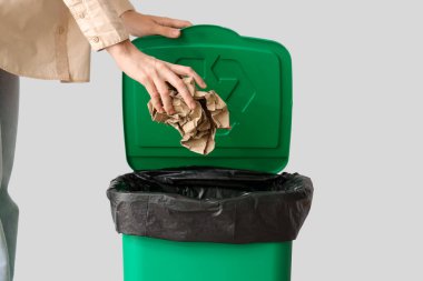 Gri duvarın yanındaki çöp kutusuna kağıt atan kadın, yakın plan.