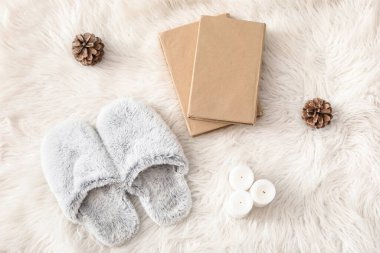 Yumuşak terlikler, mum ve kürk halısı üzerine kitaplar.