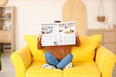 Young woman reading newspaper on sofa at home